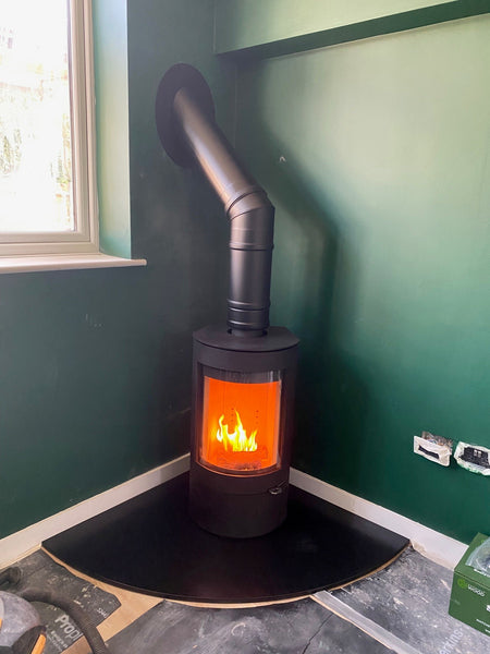 Corner design inspiration, the sleek, slim and curved Uniq 26 installed on a quadrant honed granite hearth, ideal for corner twin wall stove installations.   The extra-large glass area provides an unparalleled view of the mesmerising fire, creating a stunning interior centrepiece.